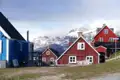Traditionelle bunte Häuser in einer grönländischen Siedlung vor der Kulisse schneebedeckter Berge.