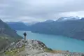 Wanderer auf einem Felsvorsprung mit Blick auf einen türkisfarbenen See und Berglandschaft.