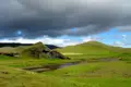 Grüne Hügellandschaft mit Fluss und dramatischem Himmel in Island.