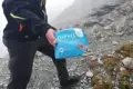 Wanderer mit einer Packung "Gipfelglück" Alpenmilch Schokolade auf einem Bergpfad.