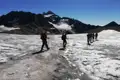 Wandergruppe mit Rucksäcken und Wanderstöcken überquert einen Gletscher in den Bergen.