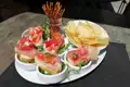 Bruschetta mit Tomaten, Schinken und Rucola, serviert mit Kartoffelchips und Salzstangen.