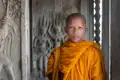 Junger Mönch in traditioneller orangefarbener Robe vor kunstvollen Steinreliefs in einem Tempel.