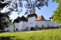 Historische Wehrkirche mit mehreren Türmen und weißer Mauer, umgeben von einer grünen Wiese.
