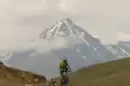 Mountainbiker auf einem Bergpfad mit schneebedecktem Gipfel im Hintergrund.