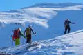 Drei Personen mit Skitouren-Ausrüstung steigen einen verschneiten Berg hinauf.