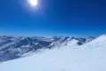 Panoramablick auf eine verschneite Bergkette unter einem klaren blauen Himmel.