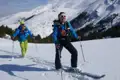 Zwei Skitourengeher mit Stöcken und Skiern in einer verschneiten Berglandschaft.