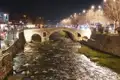 Beleuchtete Steinbrücke bei Nacht mit Fluss.