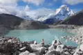 Türkisfarbener Bergsee mit schneebedeckten Gipfeln im Hintergrund.