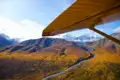 Flugzeugflügel und herbstliche Berglandschaft mit Fluss aus der Luftperspektive.