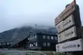 Die Sognefjellshytta, eine Berghütte in Norwegen, mit Wegweisern zu verschiedenen Wanderzielen. Nebel bedeckt die umliegenden Berge.