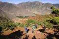 Wandergruppe auf einem Bergpfad im Atlasgebirge. Roter Boden und grüne Vegetation prägen die Landschaft.