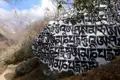 Bemalter Felsbrocken mit tibetischen Mantras auf einem Bergwanderweg.