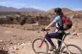 Mountainbikerin macht eine Pause auf ihrer Tour und blickt auf eine verlassene Siedlung in der Wüstenlandschaft.