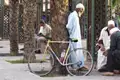 Männer in traditioneller Kleidung ruhen sich in einem Park in Marrakesch aus. Ein gelbes Fahrrad steht an einem Baum gelehnt.