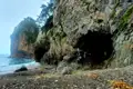 Felsige Küste mit einer Höhle und Kieselstrand.