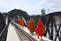 Mönche in orangefarbenen Gewändern gehen über eine Brücke mit Bahngleisen.