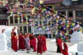 Mönche in roten Roben versammelt unter bunten Gebetsfahnen auf einem Tempelplatz.