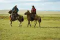 Zwei Reiter in traditioneller Kleidung durchqueren die Steppe auf ihren Pferden.