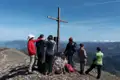 Wandergruppe am Gipfelkreuz mit Panoramablick auf die Berge.