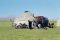 Reisende bereiten sich an einer Jurte mit Fahrrädern und einem Geländewagen auf die Weiterreise vor.