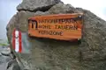 Schild mit der Aufschrift 'Nationalpark Hohe Tauern Kernzone' und rot-weiße Wegmarkierung an einem Felsen.