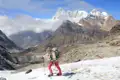 Wanderer mit Stöcken und Rucksack überquert einen verschneiten Bergpfad im Himalaya.