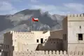 Historisches omanisches Fort mit wehender Flagge und Gebirgslandschaft im Hintergrund.