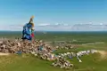 Gebetsfahnen und eine Gebetsstange auf einem Steinhaufen in der Mongolei. Im Hintergrund ist die weite Landschaft der Steppe und eine ummauerte Anlage zu sehen.