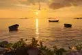 Sonnenuntergang über dem Meer mit drei Booten im Vordergrund.