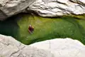 Eine Person erfrischt sich im Wasser eines natürlichen Pools inmitten einer felsigen Schlucht.