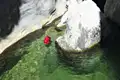 Eine rote Schwimmhilfe treibt in einem smaragdgrünen Flussbecken, das von Felsen umgeben ist.