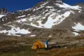 Wanderer im Basislager mit Zelt vor schneebedecktem Berg