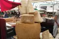 Parmesan-Käse auf einem Marktstand, möglicherweise in Parma oder Reggio Emilia, Italien. Der Käse ist in großen und kleinen Stücken zu sehen und trägt die Kennzeichnung "Parmigiano-Reggiano".