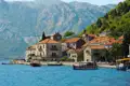 Eine malerische Küstenstadt in Montenegro, umgeben von majestätischen Bergen. Traditionelle Häuser mit roten Ziegeldächern säumen die Küste, während Boote im Hafen schaukeln.