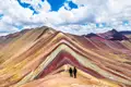 Zwei Wanderer auf dem Vinicunca, auch bekannt als Regenbogenberg, bewundern die vielfarbigen Gesteinsschichten.