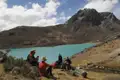 Wanderer pausieren am Ufer eines türkisfarbenen Bergsees inmitten einer bergigen Landschaft.