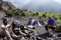 Wanderer ruhen sich im Basislager aus, umgeben von Zelten und einer felsigen Landschaft mit Bergen im Hintergrund.