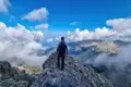 Wanderer auf einem Berggipfel mit Blick auf eine Berglandschaft und Wolken.