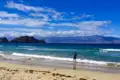 Strandansicht mit einer Person im Wasser, Inseln und Bergen im Hintergrund.