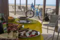 Mittagessen am Strand während einer Radtour. Ein blaues Mountainbike steht neben einem Tisch mit Essen, im Hintergrund ist das Meer zu sehen.
