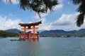 Das berühmte rote Torii des Itsukushima-Schreins, das im Wasser steht, mit Bergen im Hintergrund.