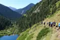 Wandergruppe auf einem Bergpfad inmitten einer bewaldeten Berglandschaft mit Blick auf einen Fluss.