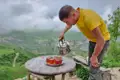 Ein Reisender schenkt Tee in Gläser ein, mit einem malerischen Blick auf das Tal im Hintergrund.