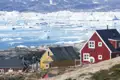 Traditionelle Häuser in einer grönländischen Küstensiedlung mit Blick auf das eisbedeckte Meer und zahlreiche Eisberge.