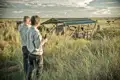 Zwei Reisende genießen den Blick auf ihre Unterkunft, eine Safari-Lodge inmitten der afrikanischen Savanne.
