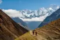 Zwei Wanderer auf einem Bergpfad im Himalaya. Im Hintergrund sind schneebedeckte Gipfel zu sehen.