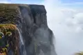 Ein Wasserfall an einer Felswand, umgeben von Wolken.