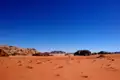 Sicht auf die rote Sandwüste mit Felsformationen und blauem Himmel.